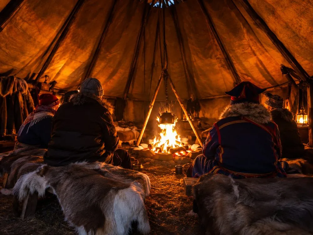 Feu brûlant à l'intérieur d'un lávvu Sámi avec des visiteurs assis autour